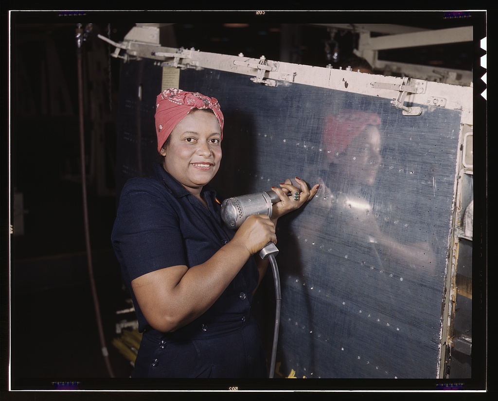 A woman operates a hand drill on a Vultee Vengeance dive bomber at the Nashville Division of Vultee Aircraft Inc., Tennessee, February 1943. Photographed by Alfred T. Palmer for the Office of War Information.